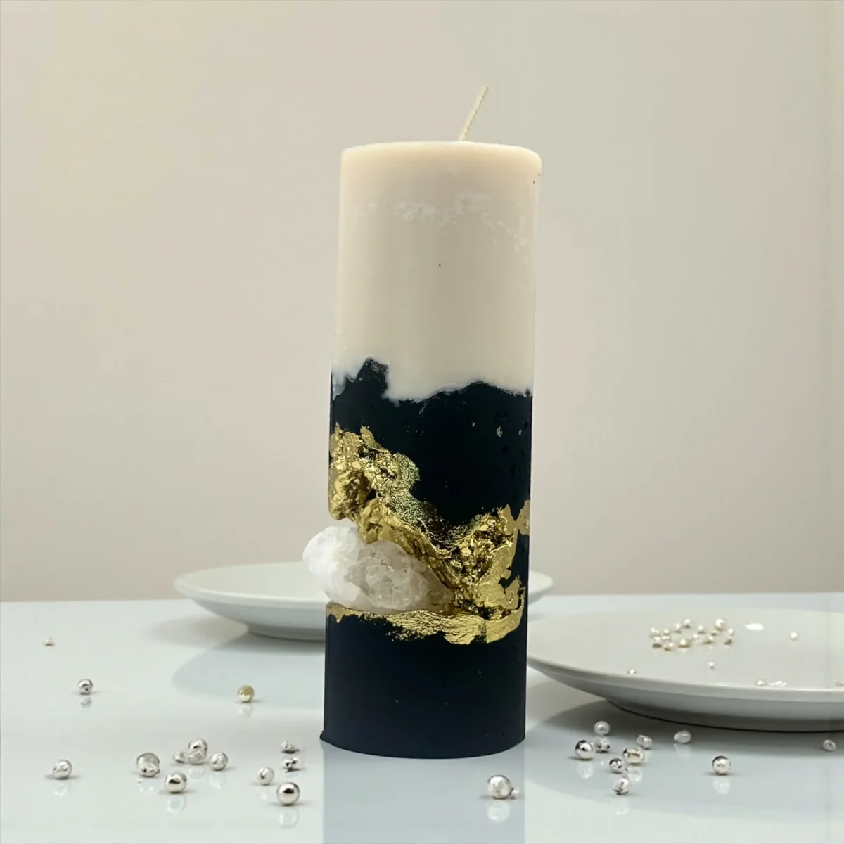Handmade luxury soy wax candle with black and ivory layers, gold leaf accents and natural crystal, displayed on a gold tray.