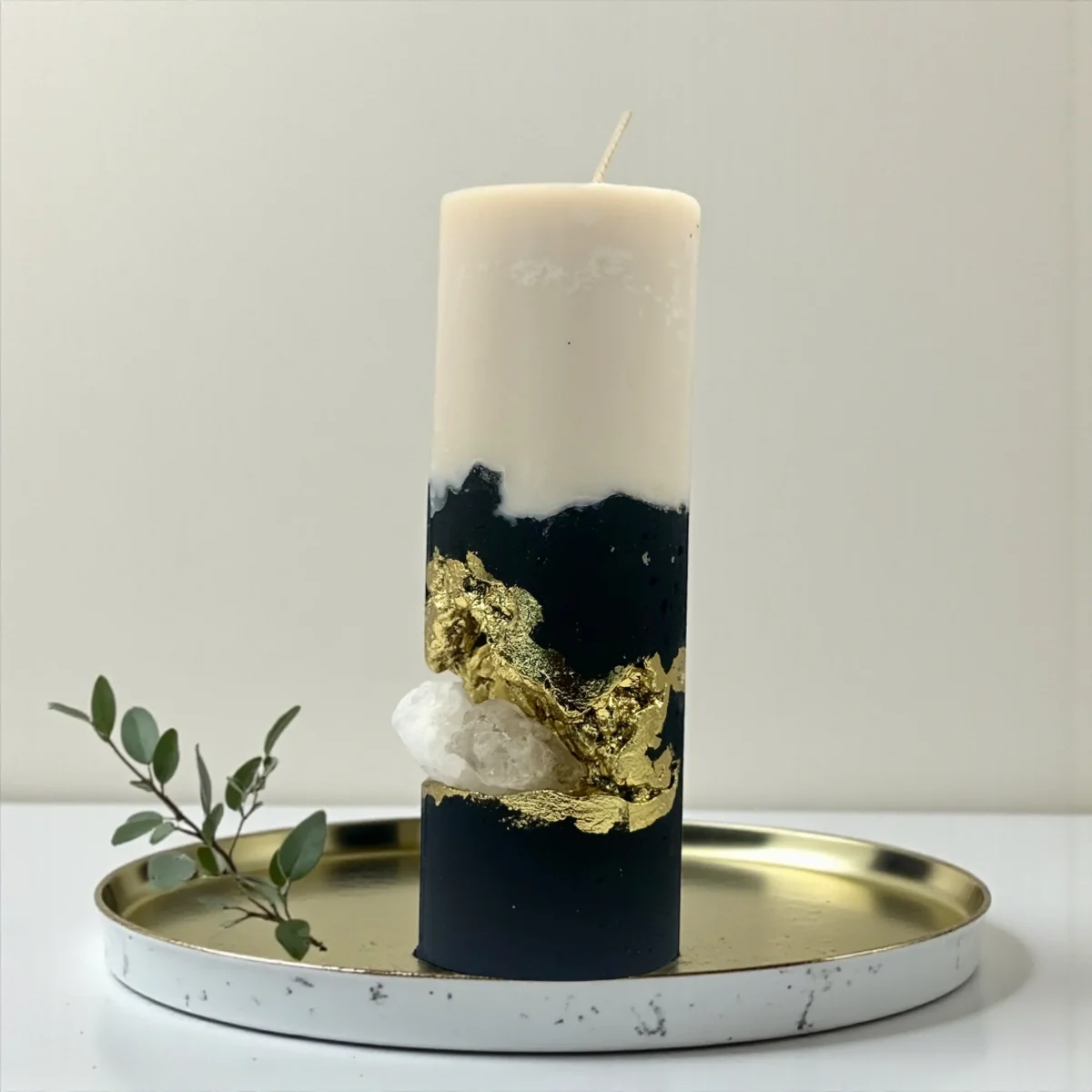 Handmade luxury soy wax candle with black and ivory layers, gold leaf accents and natural crystal, displayed on a gold tray.